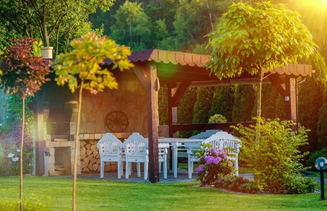 Pergola in een tuin met witte meubel tussen de bomen