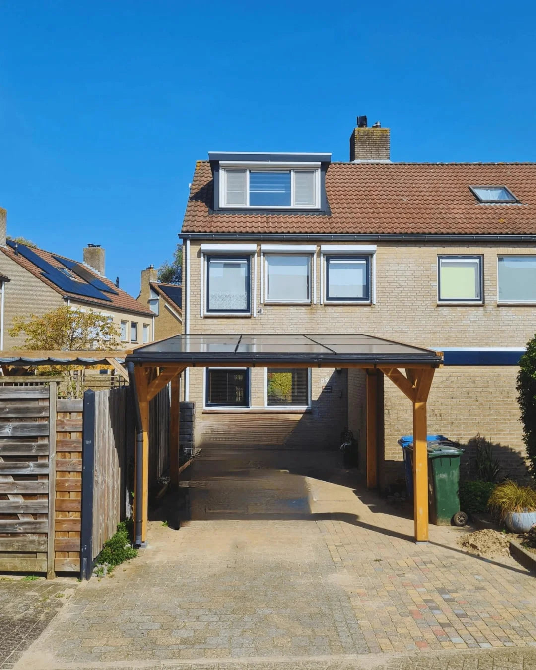 Een rijtjeshuis met een enkele carport voorzien van zonnepanelen op een zonnige dag.