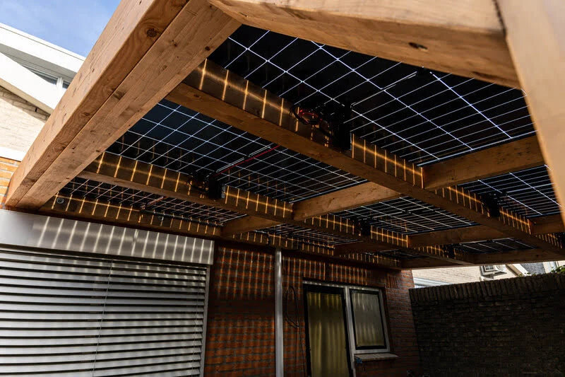 houten overkapping met zonnepanelen van onderaanzicht tegen een huis