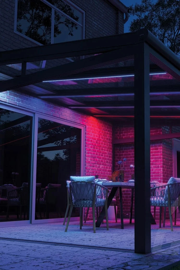 Terras met LED-verlichting in rood en blauw onder een overkapping bij nacht.