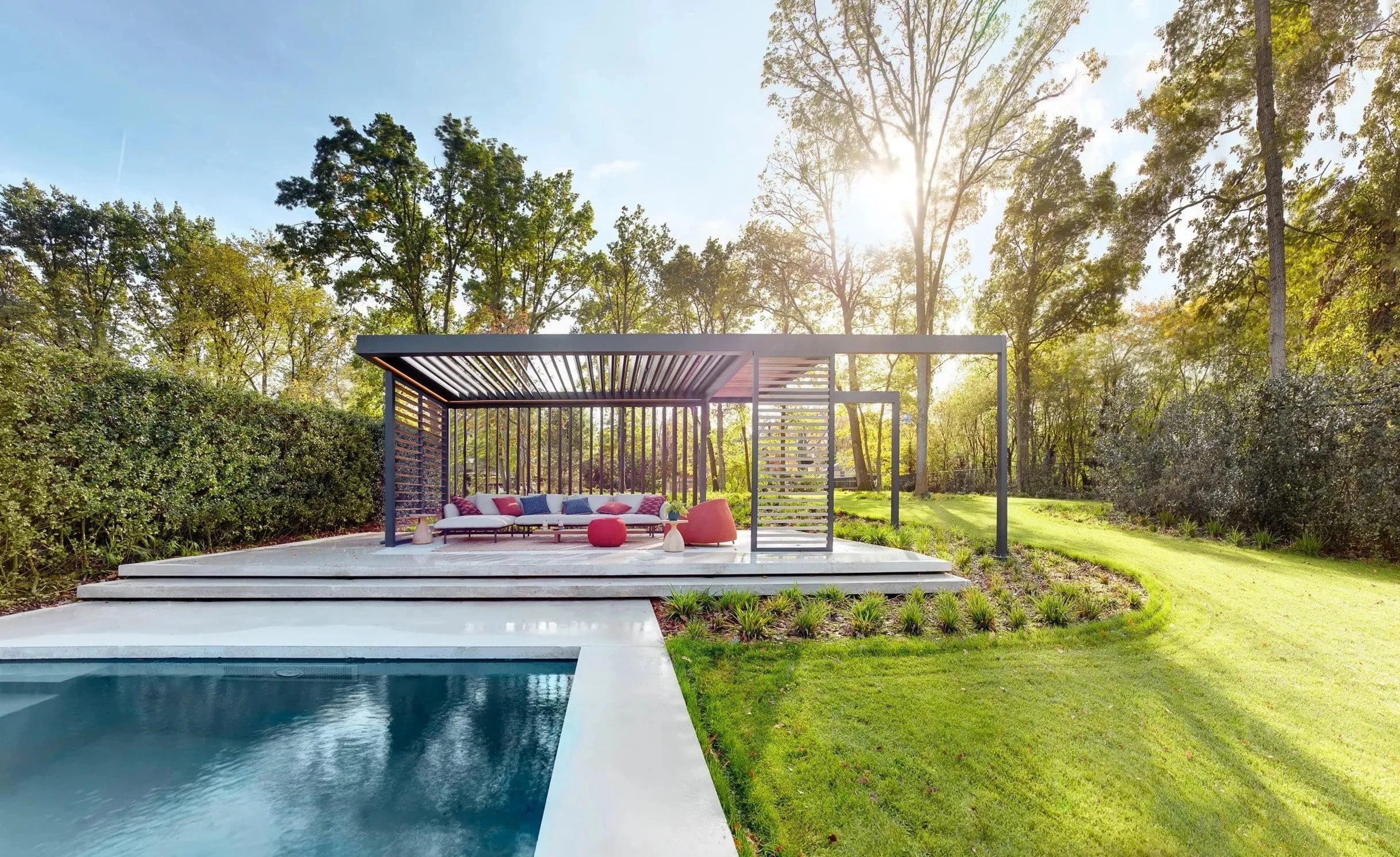 Moderne tuin met zwembad, pergola en loungeset in een natuurlijke omgeving bij zonsondergang.