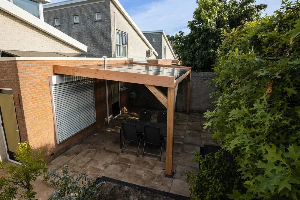 Terrasoverkapping met dak van zonnenpanelen bij een bakstenen huis en groene tuin.