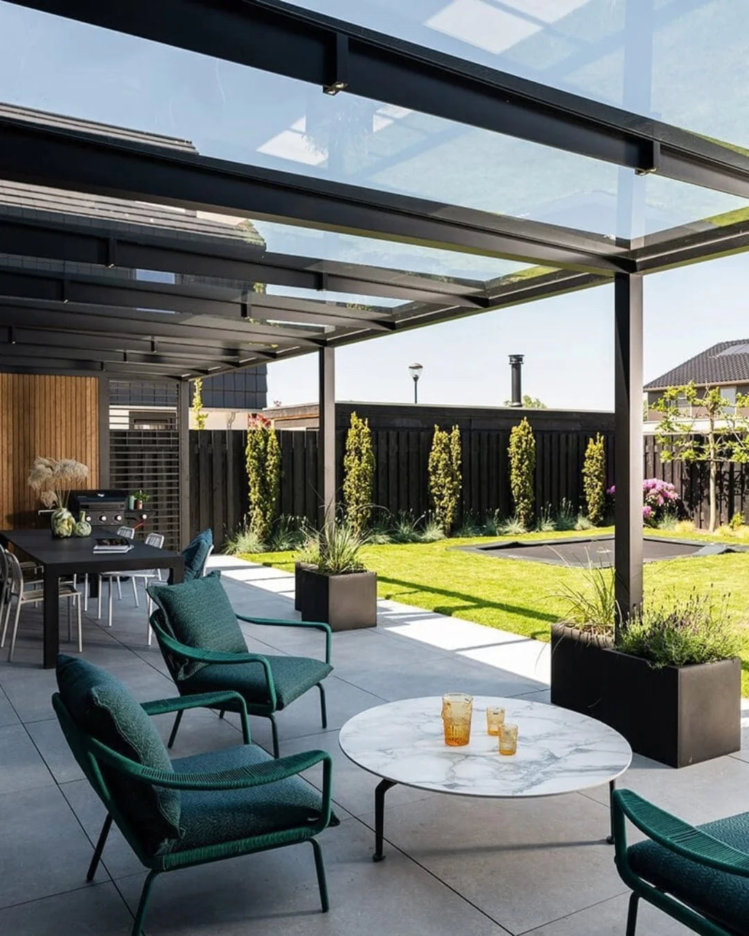 stijlvolle buitenruimte met een moderne terrasoverkapping. De overkapping heeft een metalen frame met glazen panelen waardoor natuurlijk licht binnenkomt. 